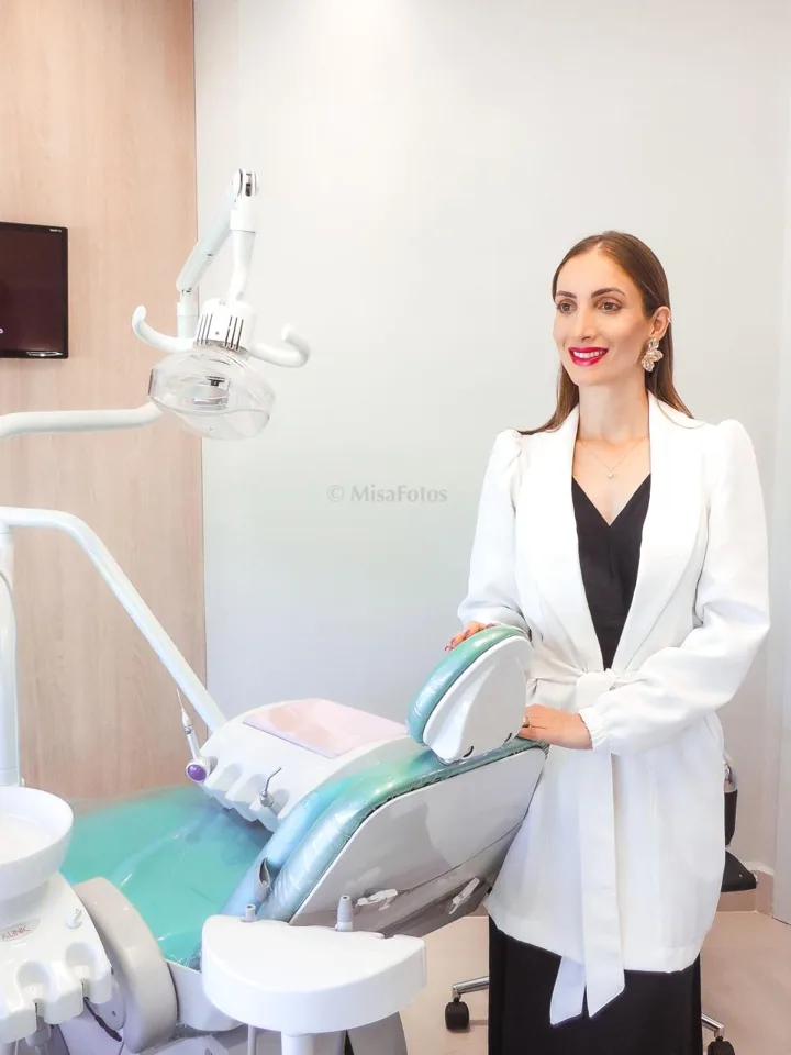 Dra. Camila ao lado da cadeira odontológica no consultório