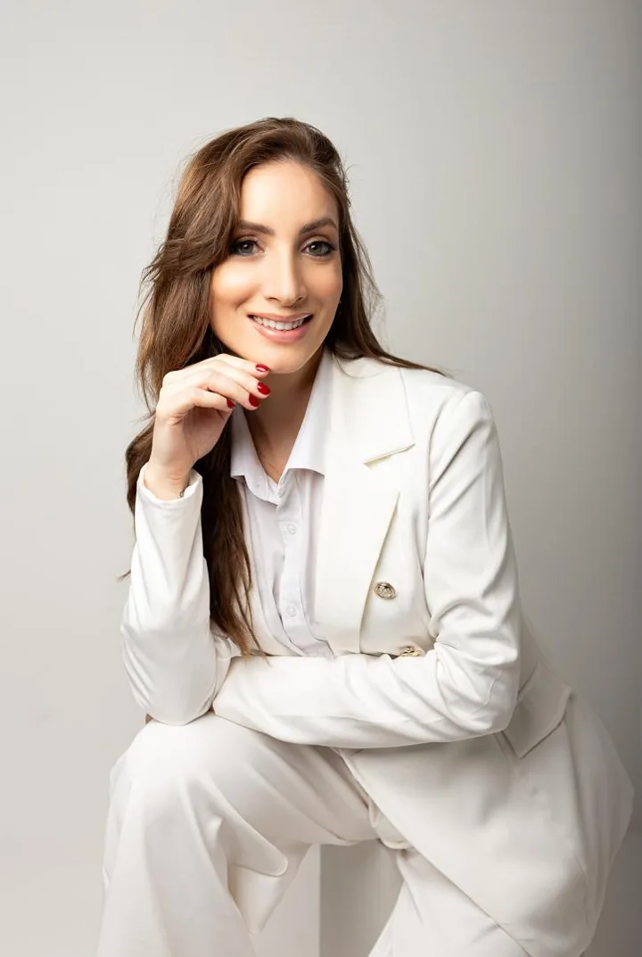 Dra. Camila de Luca sorrindo, com blazer branco